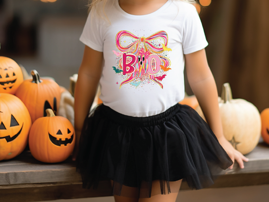 A young girl wearing a white t-shirt with a colorful graphic and a black tulle skirt stands next to a collection of carved pumpkins.