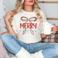 A woman sitting on a couch with a mug of hot chocolate in her hand, wearing a white t-shirt with a Christmas-themed design.