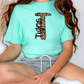 A person wearing a turquoise t-shirt with a leopard print design and gray shorts is sitting on the floor.