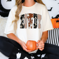 A woman wearing a white t-shirt with the word "BOWDY" printed on it, sitting on a couch with a pumpkin-shaped mug in her hands.