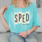 A woman wearing a turquoise t-shirt with the word "SPED" printed on it, sitting on a couch.