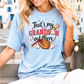 A woman wearing a light blue t-shirt with a graphic design that says "That's my GRANDSI'S OUT THERE" and features baseball-related imagery.