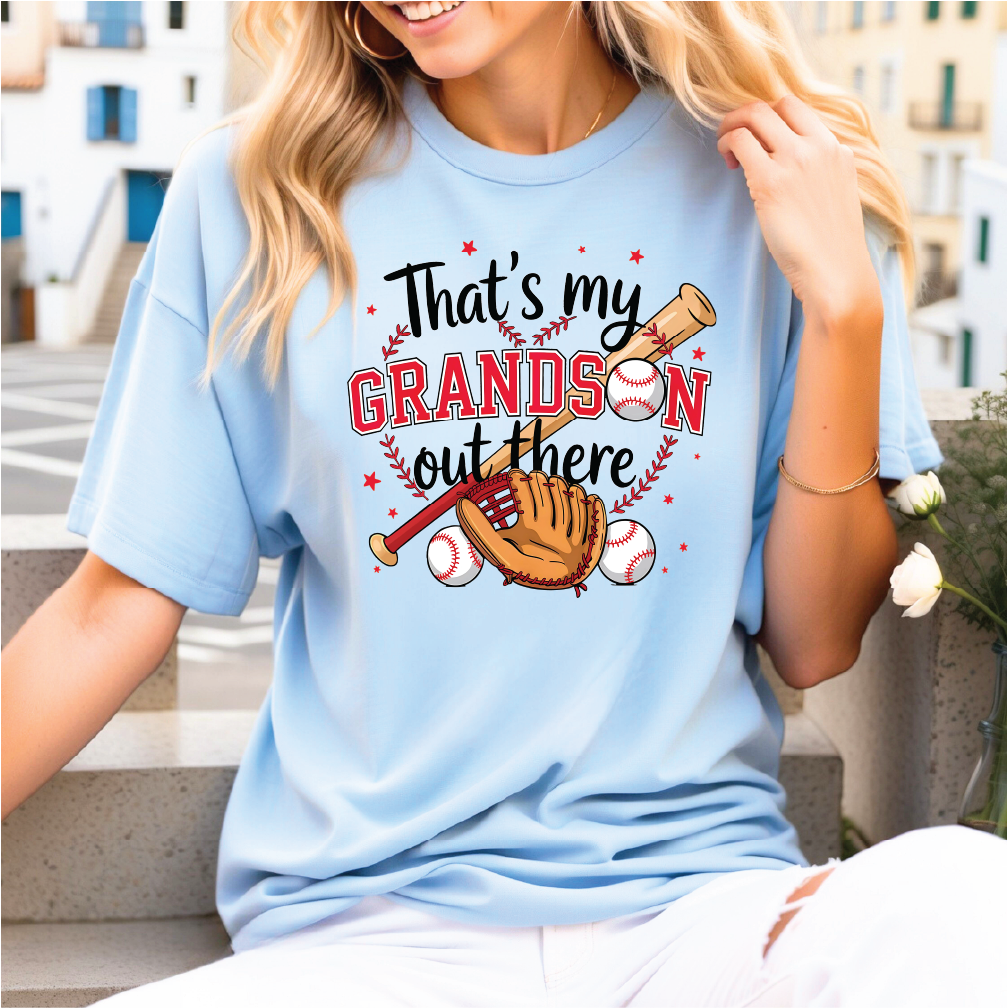 A woman wearing a light blue t-shirt with a graphic design that says "That's my GRANDSI'S OUT THERE" and features baseball-related imagery.
