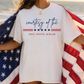 A person wearing a white t-shirt with the text "courtesy of the" printed on it, standing on a beach with an American flag draped over their shoulder.