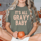 A woman wearing a green t-shirt with the text "IT'S ALL GRAVY BABY" is sitting on a bed, holding a pumpkin-shaped mug.