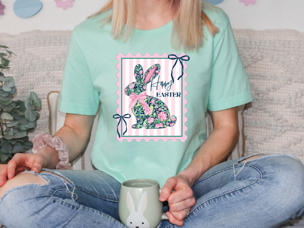 A woman wearing a green t-shirt with a floral design and the text "Happy Easter" is sitting on a couch with a mug in her hand.