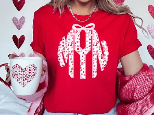 A woman wearing a red t-shirt with a monogram design and holding a white mug with a heart pattern.