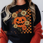 A woman wearing a black t-shirt with a pumpkin and flower design, along with a red sweater, stands against a white background with bats.