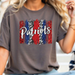 A woman wearing a gray t-shirt with the word "Patriots" printed on it, along with a patriotic design featuring red, white, and blue colors.
