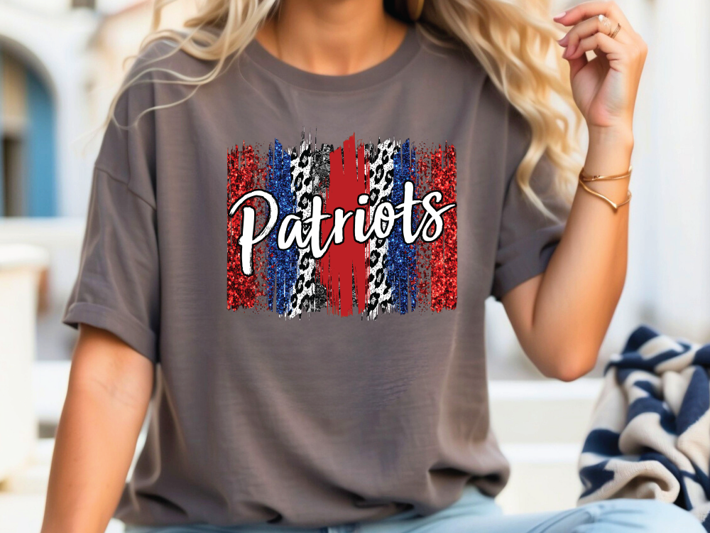 A woman wearing a gray t-shirt with the word "Patriots" printed on it, along with a patriotic design featuring red, white, and blue colors.