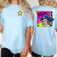 A woman wearing a light blue t-shirt with a graphic design on the back, including a cartoon character and text.