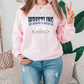 a woman in a pink sweatshirt is standing in front of a couch