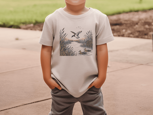 A young boy wearing a t-shirt with a printed image of ducks in a pond.