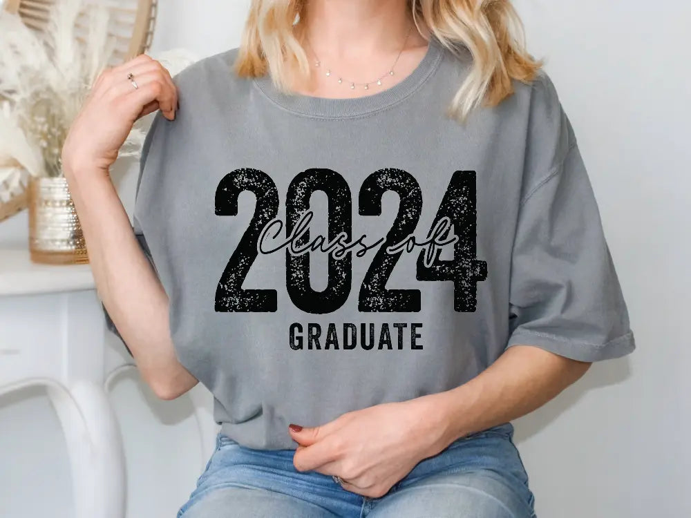 a woman sitting on a chair wearing a gray graduation t - shirt