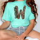 A person wearing a turquoise t-shirt with a leopard print design and gray shorts is sitting on the floor.