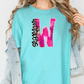 A woman wearing a turquoise t-shirt with a pink and black graphic design on it, and a denim jacket.