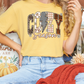 A person wearing a yellow t-shirt with the word "COZY" printed on it, sitting on a couch with a red blanket and a pumpkin decoration.