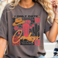 A woman wearing a grey t-shirt with a graphic design featuring various cowboy-related elements such as a cowboy hat, boots, and a cactus.