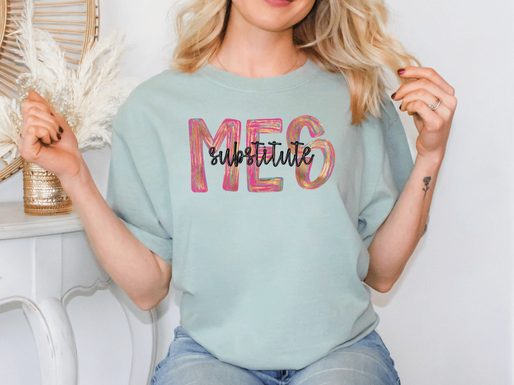 A woman wearing a light blue t-shirt with the text "MES" printed on it, sitting in front of a white wall with a decorative item behind her.