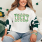 A woman wearing a white shirt with the word "Lucky" printed on it, sitting on a couch with a green and white patterned blanket.