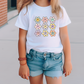 a little girl standing on a sidewalk wearing a t - shirt with flowers on it