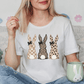 A woman wearing a white t-shirt with a graphic of three cartoon rabbits, one with a checkered pattern and the other two with leopard print, is sitting on a couch with a mug in her hand.