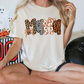 A woman wearing a white t-shirt with the word "MOM" printed on it, sitting cross-legged on the floor. There are Halloween decorations and ghost figures in the background.