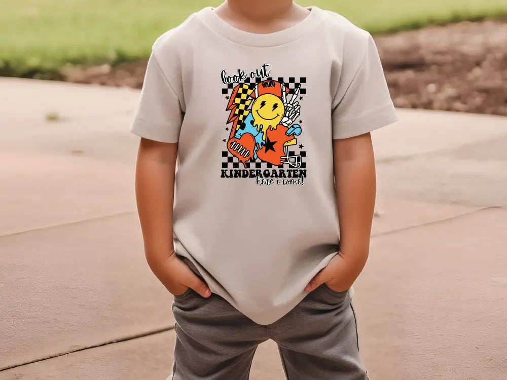 a young boy standing on a sidewalk wearing a t - shirt