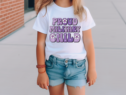 a little girl standing on a sidewalk wearing a shirt that says proud military child