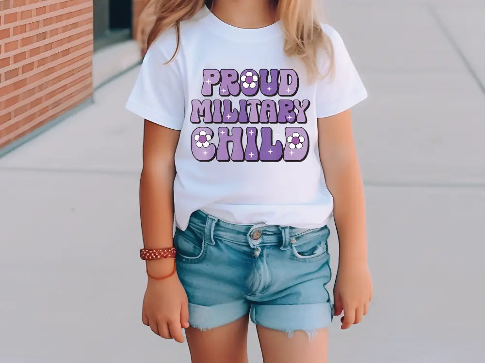 a little girl standing on a sidewalk wearing a shirt that says proud military child