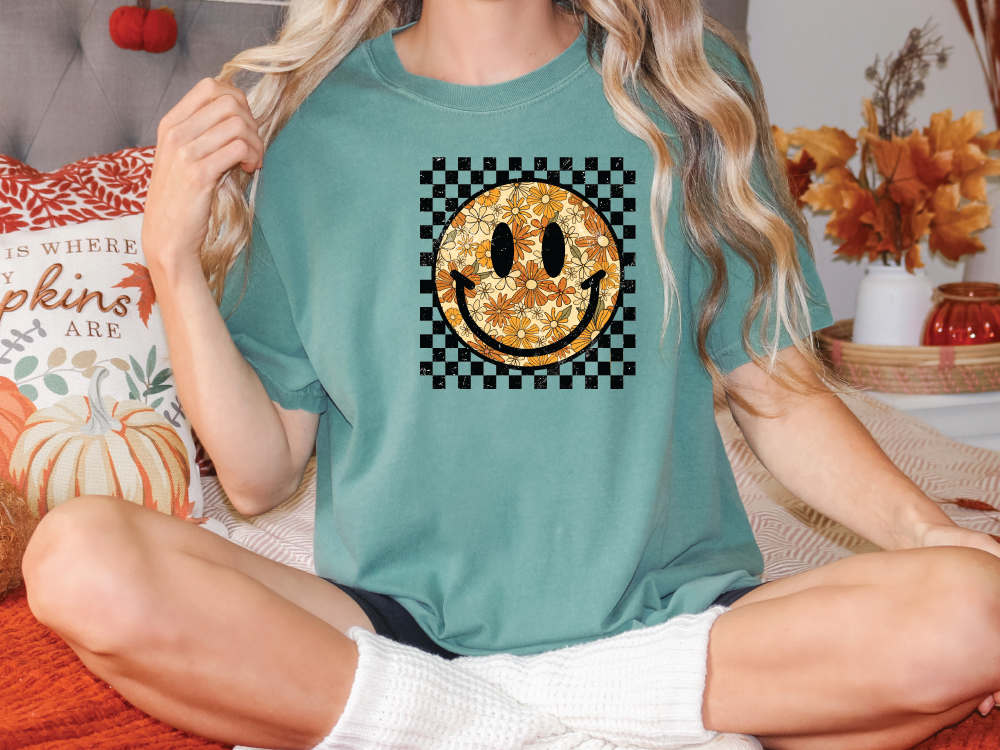 a woman sitting on a bed wearing a t - shirt with a smiley face on