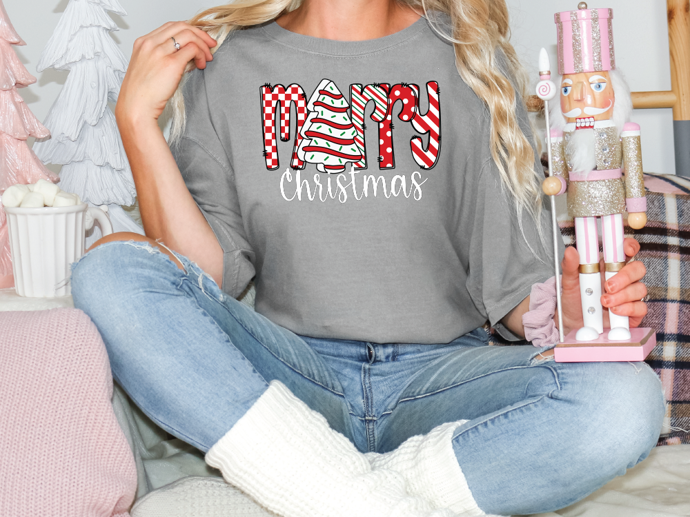 a woman sitting on a bed holding a christmas t - shirt