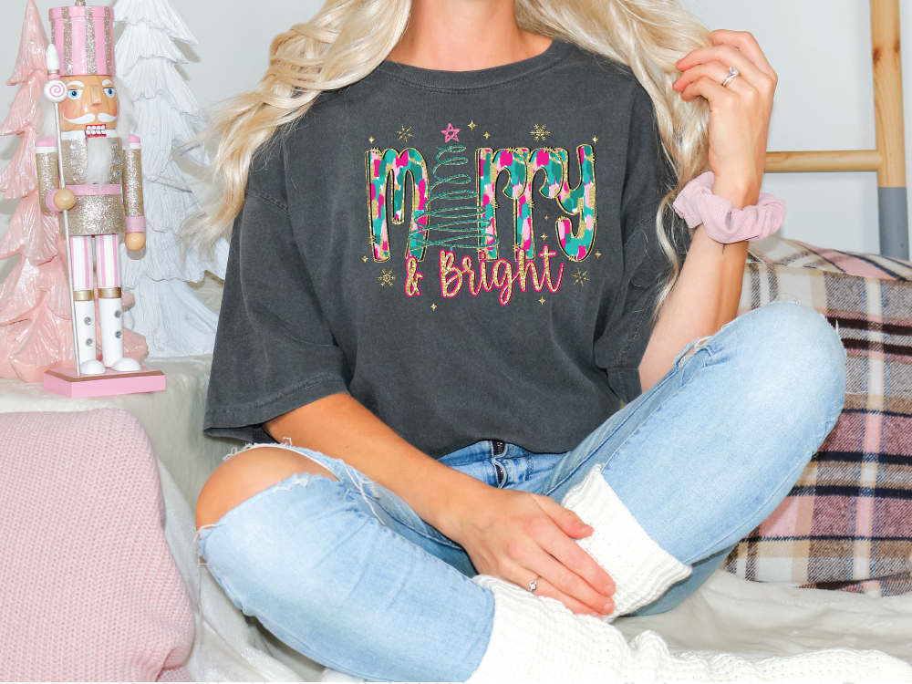 a woman sitting on a bed wearing a black merry and bright shirt