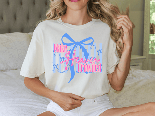 A woman wearing a white t-shirt with a graphic design and text, sitting on a bed.