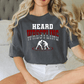A woman wearing a gray t-shirt with the text "HEARD WRESTLING" and a graphic of two wrestlers.