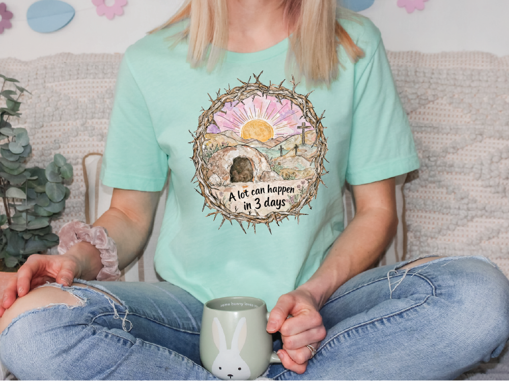 A woman wearing a green t-shirt with a graphic design sits on a chair, holding a mug with a bunny face on it.