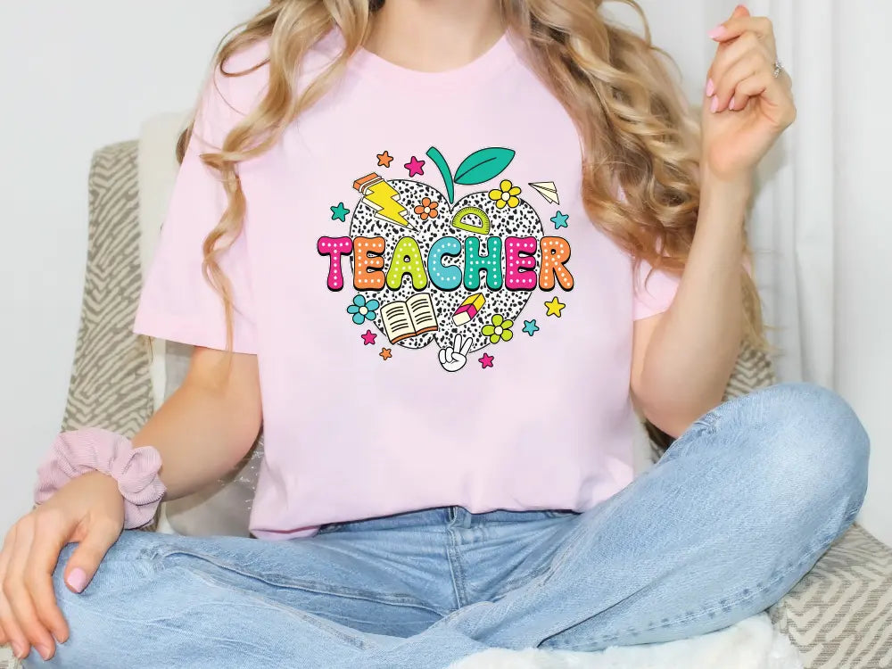 a woman sitting on a chair wearing a pink teacher shirt