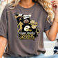A woman wearing a gray t-shirt with a graphic design featuring various sports-related elements, including a bee, football, and cheerleaders.