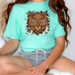 A person wearing a turquoise t-shirt with an owl graphic and gray shorts is sitting cross-legged on the floor.