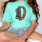 A person wearing a turquoise t-shirt with a leopard print design and gray shorts is sitting on the floor.