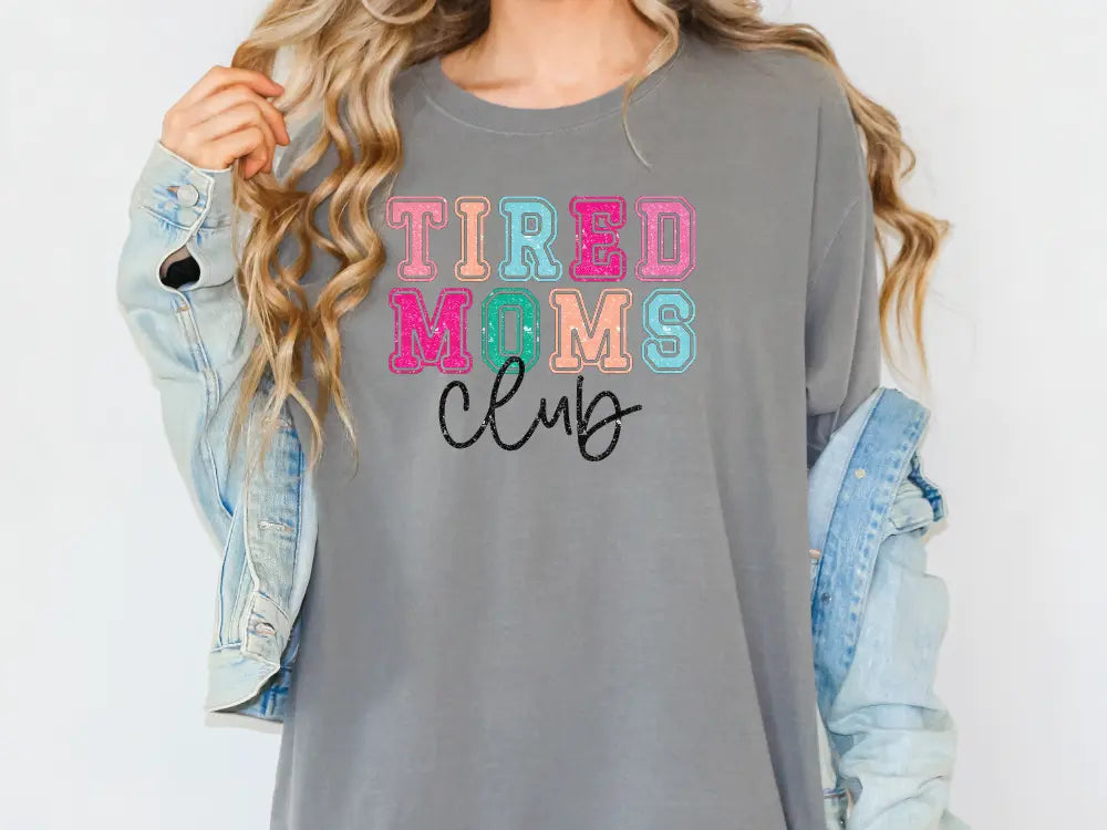 a woman wearing a gray shirt that says tired moms club