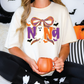 A woman wearing a white t-shirt with a Halloween-themed design is sitting on a couch, holding a pumpkin-shaped mug.