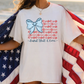 A person wearing a white t-shirt with a graphic design of an American flag and the text "land that I love" printed on it, holding the flag in their arms.