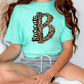 A person wearing a turquoise t-shirt with a leopard print design and gray shorts is sitting on the floor.