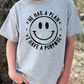 A person wearing a gray t-shirt with a black smiley face design and text around it.