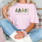 a blonde woman sitting on a bed wearing a pink merry and bright t - shirt