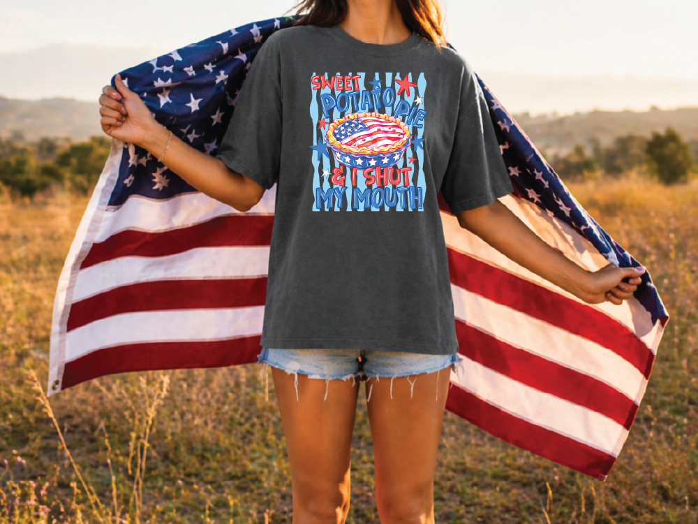 A person standing in a field holding an American flag, wearing a gray t-shirt with a graphic design.