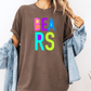 A person wearing a brown t-shirt with the word "BEARS" in colorful letters, along with a denim jacket, stands against a white background.