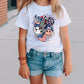 a little girl standing on a sidewalk wearing a t - shirt with a picture of