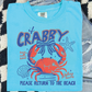 A blue t-shirt with a crab design and text, placed on a checkered surface.